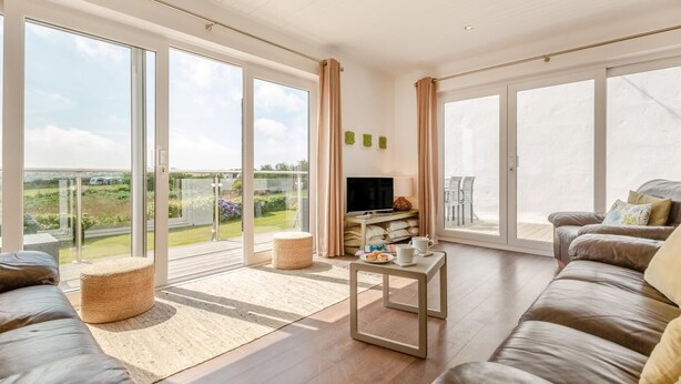 A spacious living room with large sliding glass doors, a flat-screen TV, a sofa, and a coffee table. - 3 Bed in Abersoch (oc-4ynysf) (Abersoch)