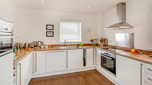 A modern kitchen with white cabinets, a stainless steel range hood, a built-in oven, and a wooden countertop. - 3 Bed in Abersoch (oc-4ynysf) (Abersoch)