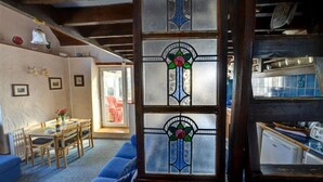 Una stanza accogliente con soffitto in legno, un'area pranzo con tavolo e sedie, e un'ampia finestra con vetri colorati.