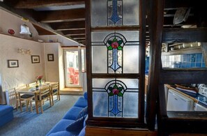 A cozy room with a wooden ceiling, a dining area with a table and chairs, and a large window with stained glass. - 3 Bed in Llanfairpwllgwyngyll (oc-wai194) (Brynsiencyn)