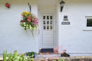 A white building with a white door, a hanging flower basket, a black lantern, and a sign that reads "BLOCHDY". - 3 Bed in Llanfairpwllgwyngyll (oc-wai194) (Brynsiencyn)