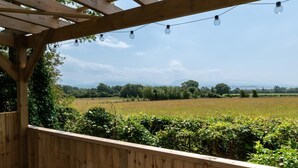 Una pergola in legno con luci a tendina, affacciata su un campo e alberi.