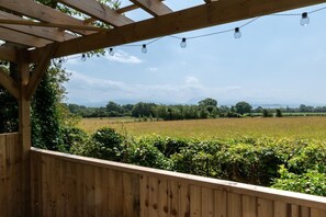 A wooden pergola with string lights, overlooking a field and trees. - 3 Bed in Llanfairpwllgwyngyll (oc-wai194) (Brynsiencyn)
