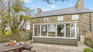 A stone house with a large glass window, a stone wall, and a wooden table. - 4 Bed in Aberdaron (oc-fl055) (Aberdaron)