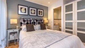 Een keurig opgemaakte slaapkamer met een bed, nachtkastjes, een kledingkast en ingelijste foto’s aan de muur.