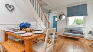 Een eetgedeelte met een houten tafel gedekt voor vier personen, een trap, een blauwe deur en een raam met uitzicht op groen.
