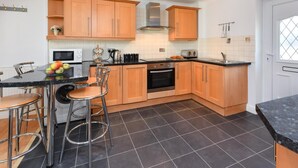Een moderne keuken met houten kastjes, een zwart aanrecht en een eethoek met barstoelen.
