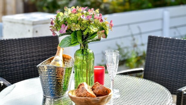 Een ronde tafel met een glazen vaas met bloemen, een fles, een glas en een schaal met brood.