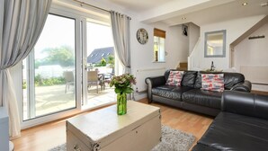 Een woonkamer met een bank, een salontafel en een koffer. Er is een raam met gordijnen, een radiator en een spiegel aan de muur.
