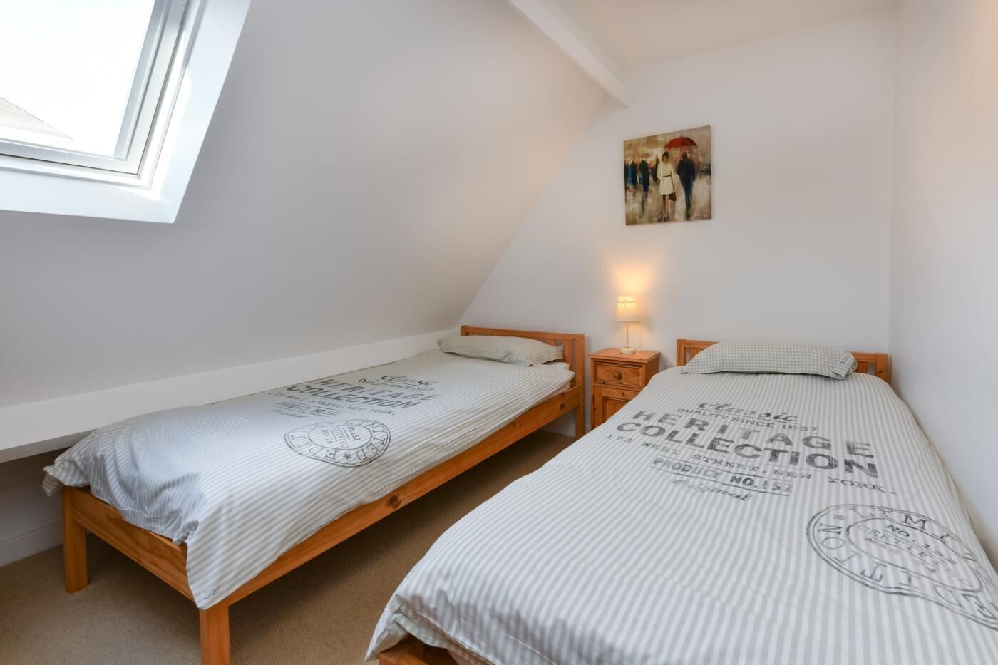 Een ruime, goed verlichte slaapkamer met twee eenpersoonsbedden, een nachtkastje met een lamp en een schilderij aan de muur.