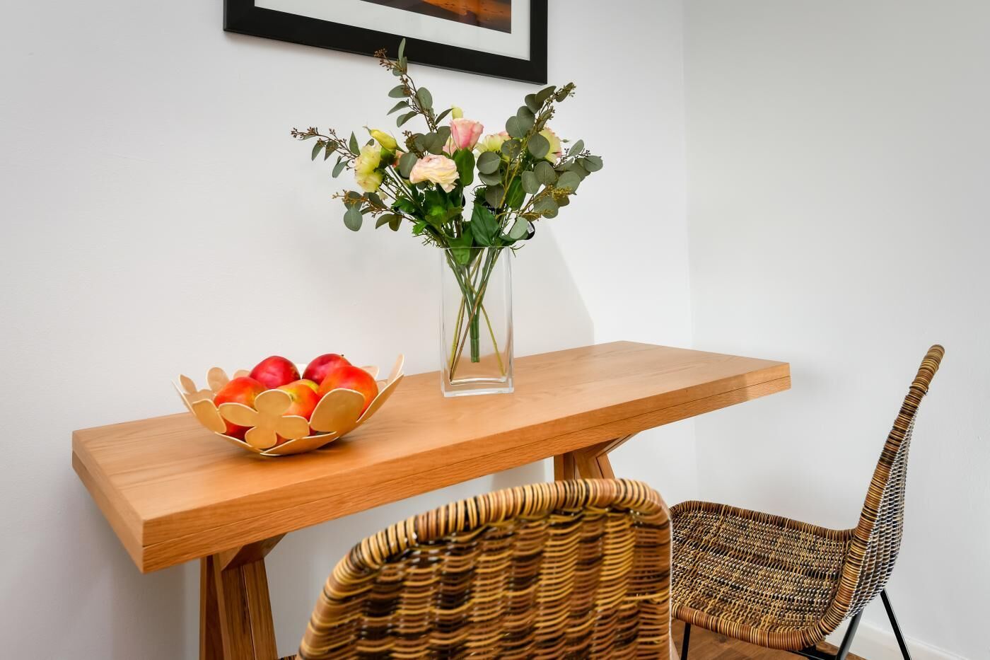 A wooden table with a vase of flowers and a bowl of fruit.