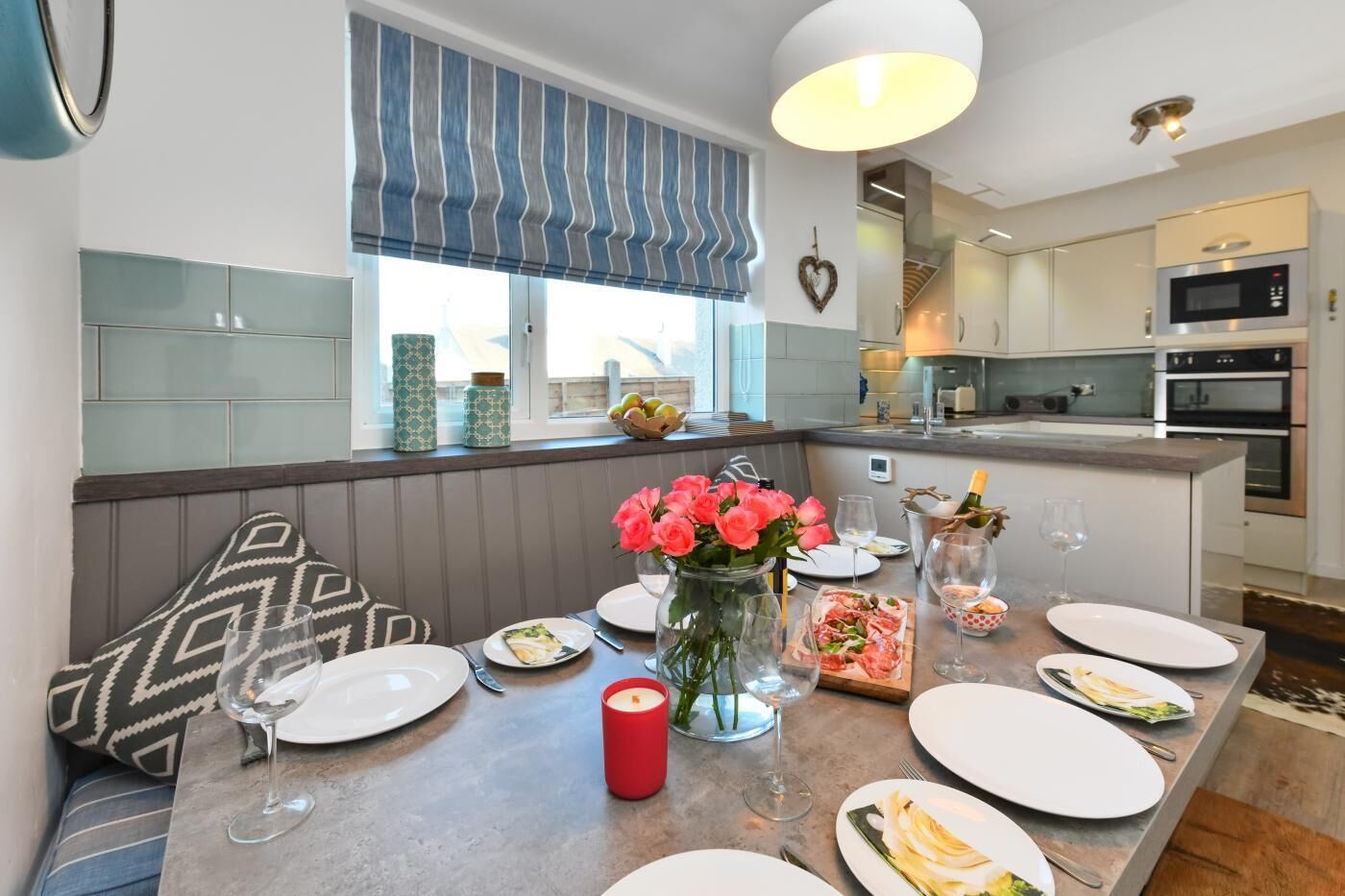 A modern kitchen with a dining area, featuring a built-in island with a vase of flowers, a candle, and a bottle of champagne.