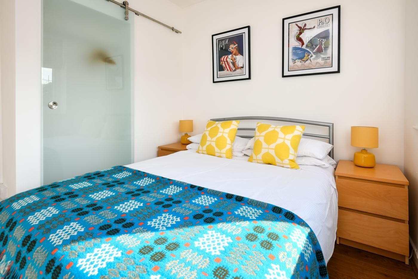 Ein Schlafzimmer mit einem Bett, zwei Nachttischen, einer Glastür und zwei gerahmten Bildern an der Wand.