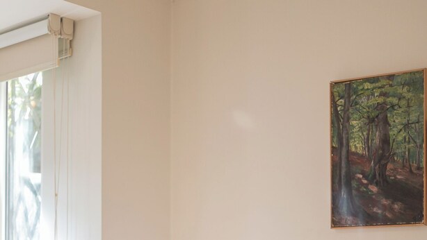 Ein Schlafzimmer mit Bett, Nachttisch, Lampe, einem Fenster mit Jalousien und einem Bild an der Wand.
