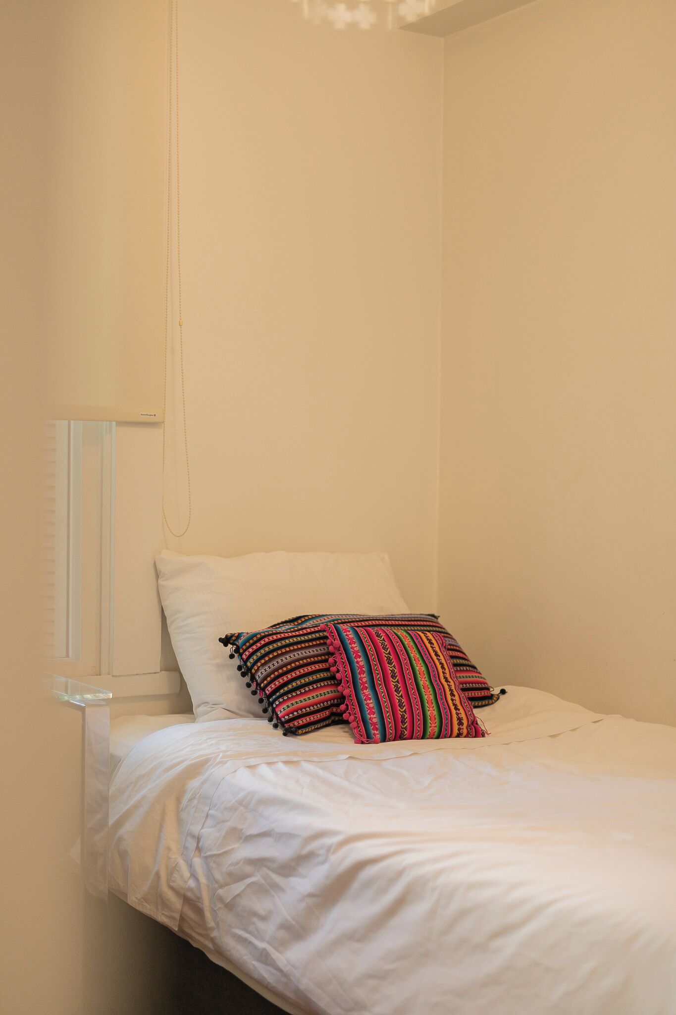 Una cama individual con ropa blanca y un cojín a rayas de colores.