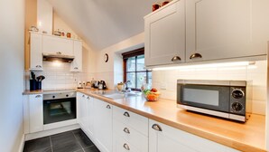 Eine moderne Küche mit weißen Schränken, einer Holz Arbeitsplatte, einem eingebauten Backofen, einer Mikrowelle und einem Fenster, das für natürliches Licht sorgt.