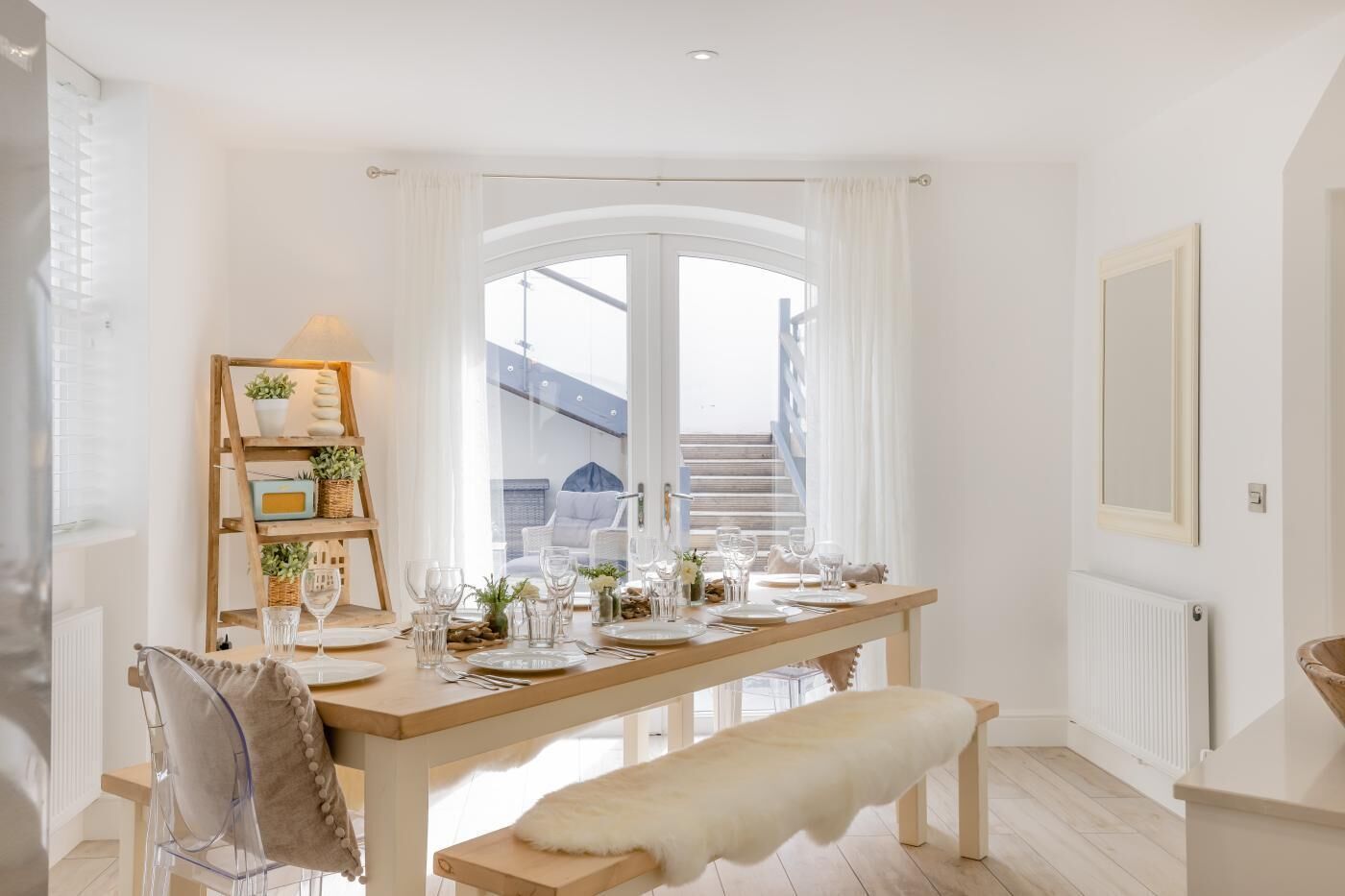 A dining area with a wooden table set for a meal, a bench, and a shelf with decorative items.