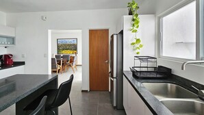 Een moderne keuken met een koelkast, spoelbak en barstoelen. Een eethoek met tafel en stoelen is in de achtergrond zichtbaar.