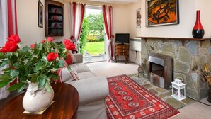 Ein Wohnzimmer mit Kamin aus Stein, einer Couch, einem roten Teppich und einer Vase mit roten Rosen.
