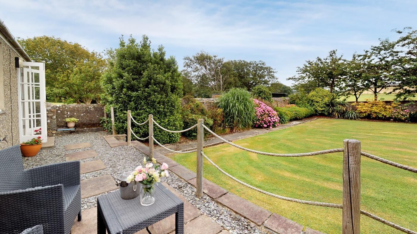 Un espace patio aménagé avec du mobilier d’extérieur, un jardin avec différentes plantes et fleurs, et une clôture en bois.
