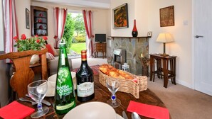 Ein Essbereich mit einem Tisch, gedeckt für zwei Personen, mit einer Flasche grünem Sekt, einer Flasche Rotwein und einem Brotkorb.
