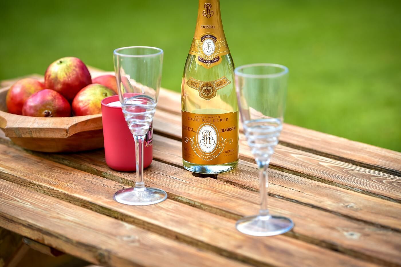 Eine Flasche Cristal Champagner, zwei Gläser und eine Schale mit Äpfeln auf einem Holztisch.
