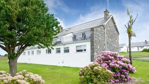A white building with a stone facade, multiple windows, and a balcony. - 2 Bed in Pwllheli (oc-45caed) (Abersoch)
