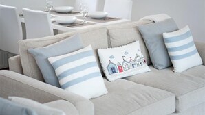 A beige sofa with striped pillows and a decorative pillow with a seaside scene. - 2 Bed in Pwllheli (oc-45caed) (Abersoch)