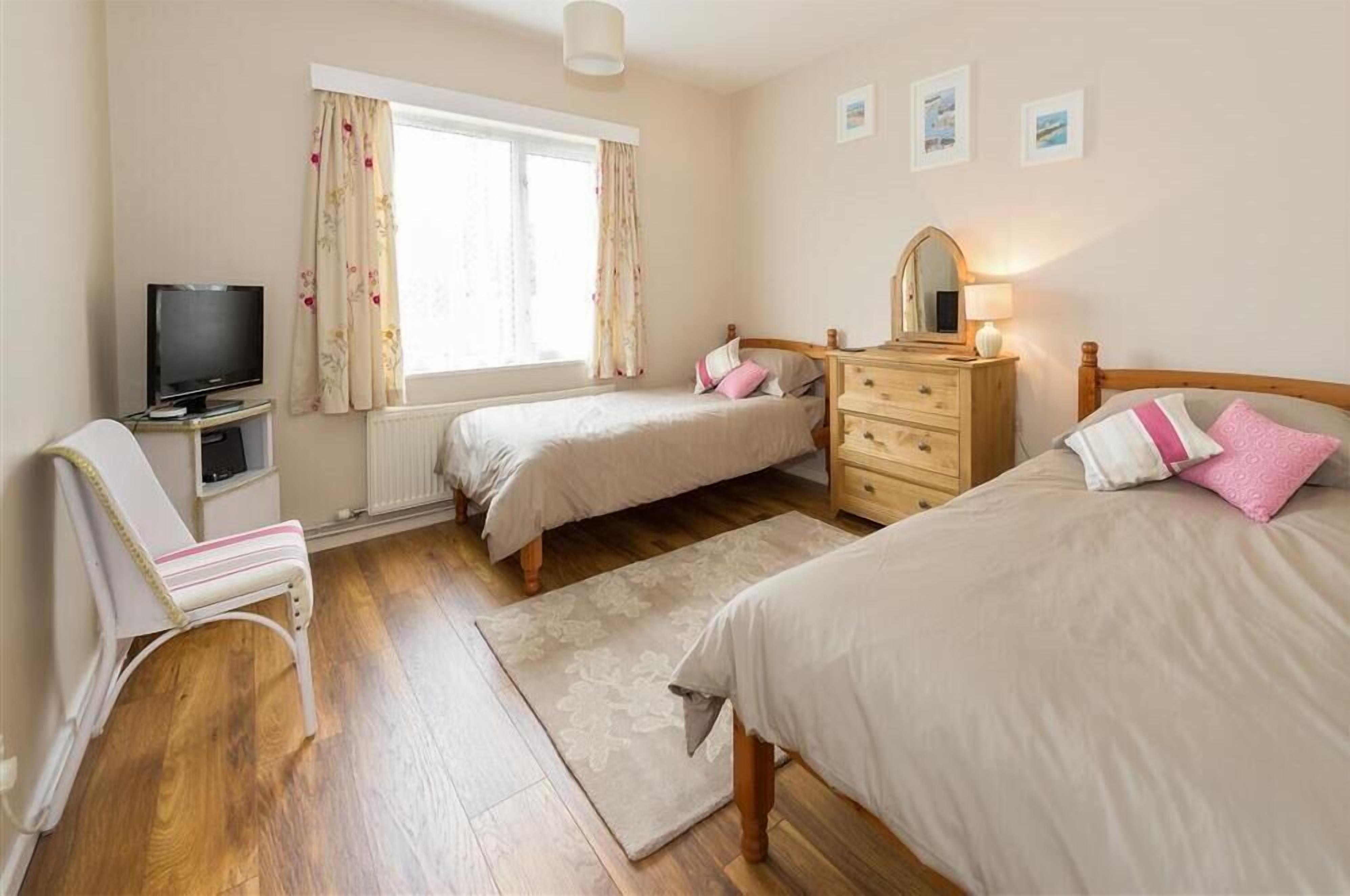 A bedroom with two beds, a TV, a dresser, and a window with curtains.