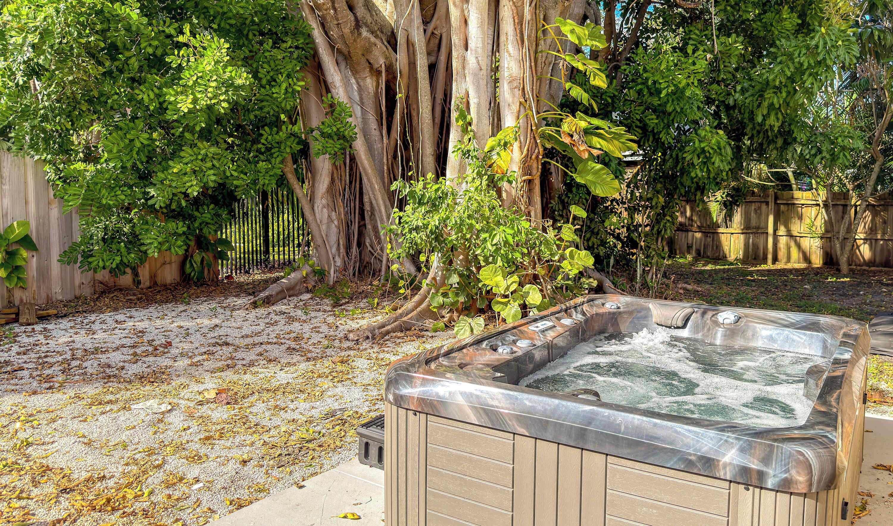 Un bain à remous dans un jardin, avec une clôture en bois, des arbres et un chemin de gravier.