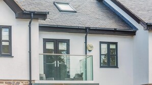 Een huis met een stenen fundering, een pannendak en een glazen deur die uitkomt op een balkon.
