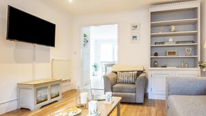 Een woonkamer met een flatscreen televisie, een open haard, een bank, een salontafel met een bord eten en een boekenkast.