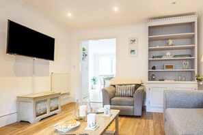 A living room with a flat-screen TV, a fireplace, a sofa, a coffee table with a plate of food, and a bookshelf. - 4 Bed in Pwllheli (oc-watern) (Abersoch)