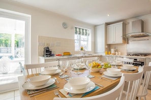 A modern kitchen with white cabinetry, a dining table set for four, and a view of the outdoors. - 4 Bed in Pwllheli (oc-watern) (Abersoch)