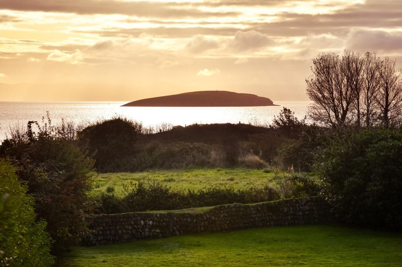 A coastal landscape with a grassy area, a stone wall, and a distant island.