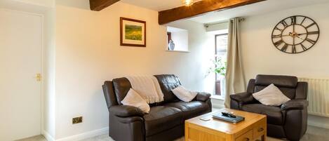 A living room with a brown leather sofa, a wooden coffee table, and two leather armchairs.