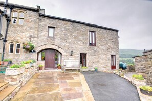 A stone building with a central entrance, a bench, and flower planters. - 2 Bed in Gunnerside (oc-ds230) (Gunnerside)