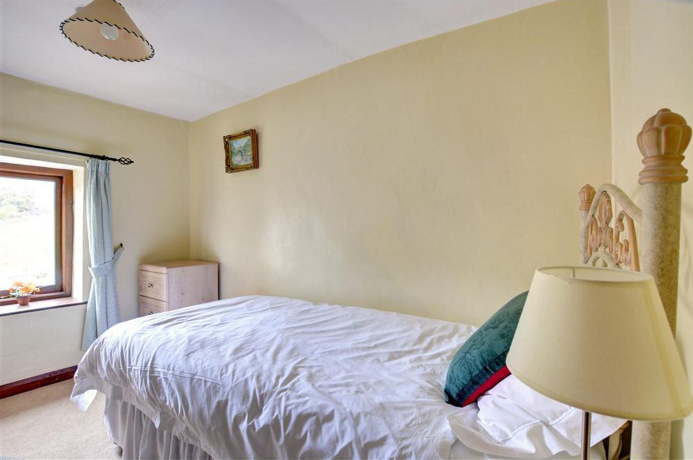 A bedroom with a bed, a nightstand, a lamp, a window with curtains, and a picture on the wall.