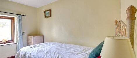 A bedroom with a bed, a nightstand, a lamp, a window with curtains, and a picture on the wall.