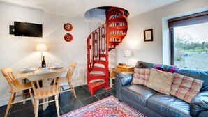 A modern living room with a spiral staircase, a dining area with wooden chairs, a sofa with plaid cushions, and a TV mounted on the wall.