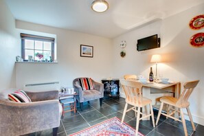 A cozy living room with a fireplace, comfortable seating, a dining area, and a flat-screen TV mounted on the wall.
