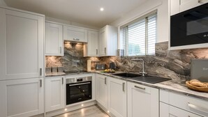 Una cocina moderna con armarios blancos, horno empotrado, pileta de acero inoxidable y salpicadero de mármol.