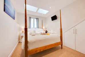 A modern bedroom with a four-poster bed, a skylight, a flat-screen TV, and a wardrobe. - 4 Bed in Thornham (oc-769) (Thornham)