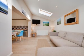 Ein modernes Wohnzimmer mit einer Couch, einem Essbereich mit Tisch und Stühlen, einer Küche mit kariertem Fliesenspiegel und Kunstwerken an den Wänden.