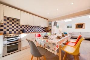 A modern kitchen with a checkered backsplash, a dining table set for four, and a sofa in the adjacent living area. - 4 Bed in Thornham (oc-769) (Thornham)