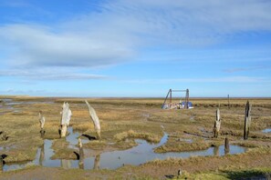 A flat landscape with a wooden structure and a blue vehicle. - 4 Bed in Thornham (oc-769) (Thornham)