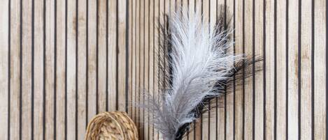 A wooden wall with vertical planks and a framed mirror. A black vase with white feathers and a woven basket are placed on a wooden surface.