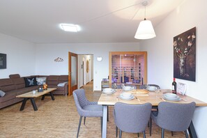 Ein modernes Wohnzimmer mit einer Couch, einem Couchtisch und einem Essbereich mit Tisch für vier Personen.
