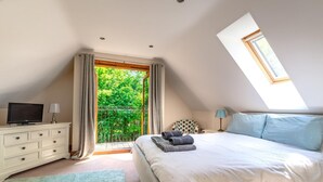 A bedroom with a bed, a TV, a dresser, and a balcony with a view of greenery. - 4 Bed in Fakenham (oc-1261) (Thursford)