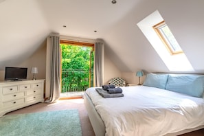 Ein Schlafzimmer mit Bett, Fernseher, Kommode und einem Balkon mit Blick auf Grünflächen.